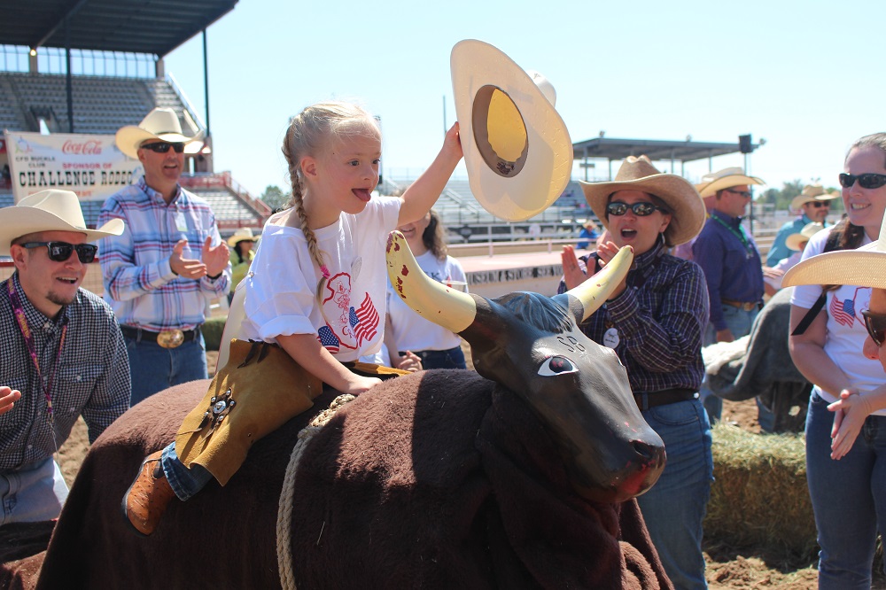 A little girl rides on a training bull as others cheer her on at the Challenge Rodeo in the Cheyenne Frontier Days arena.