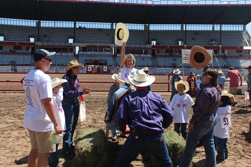 A young teen raises her cowboy hat as she rides a training bull at the challenge rodeo in the Cheyenne Frontier Days arena.