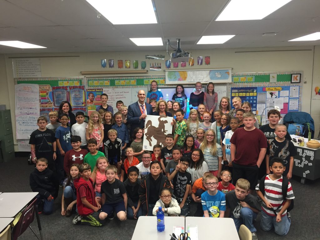 State Superintendent Jillian Balow and WDE Chief of Staff Dicky Shanor hold up a large signed poster surrounded by 5th grade students and their teachers.