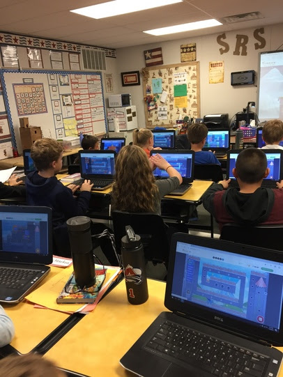 A classroom of 4th grade students each sit at a laptop participating in an online program that teaches coding.
