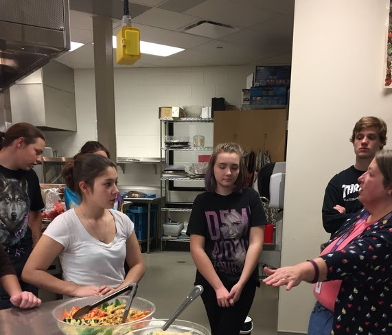 A culinary arts teacher addresses her students in the kitchen.