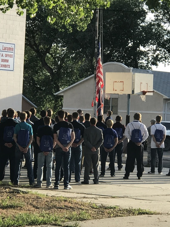 A group of boys state delegates stand at attention outside in front of a flagpole as the U.S. and Wyoming flags are lowered.