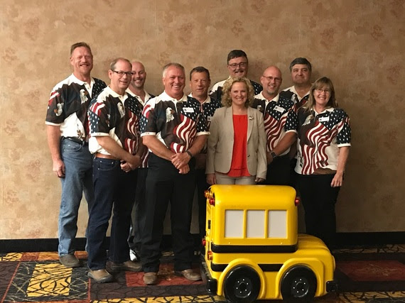 Superintendent Balow stands with transportation conference participants near a small remote-controlled school bus.