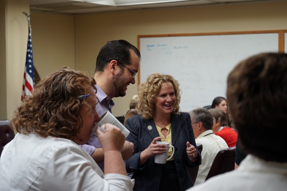 Superintendent Balow visits with employees in a conference room while they all enjoy coffee.