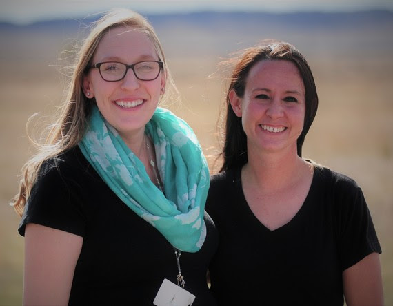 Valerie Bruce and Sara Reed pose next to each other outside Valerie's school with the Wyoming prairie in the background.