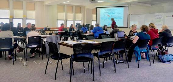 A classroom full of teachers look at a screen where Cindy and Sharla lead training on the new science standards.