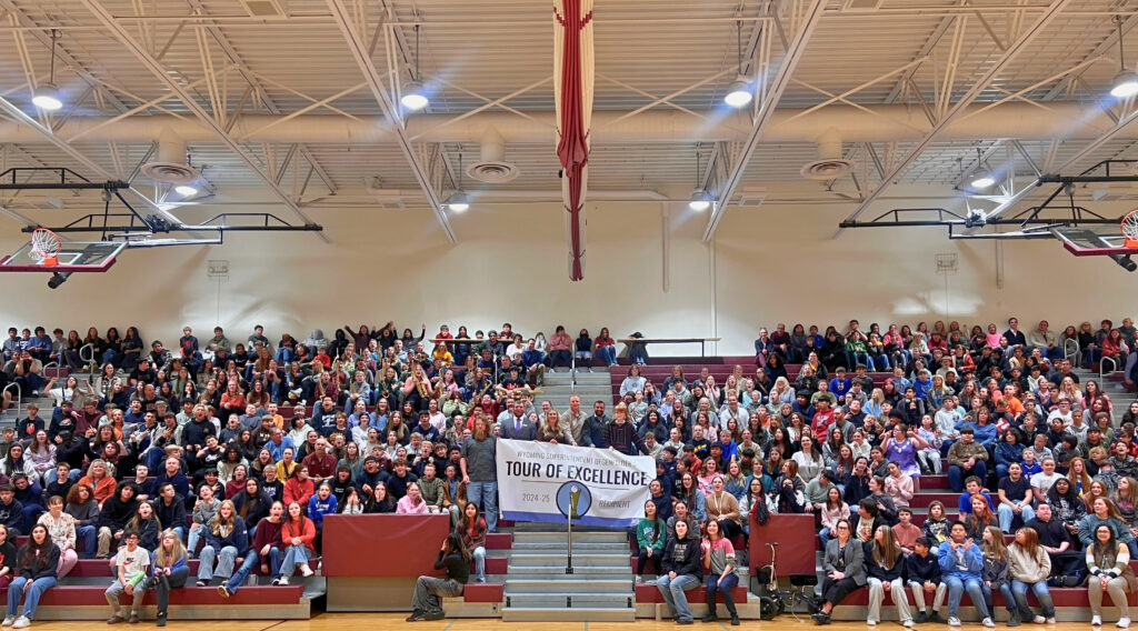 Members of the Wyoming Department of Education hold a, "Tour of Excellence" banner on bleachers full of Riverton Middles School students and staff.